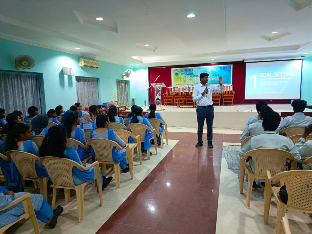Photo of PCS Board member, Aravindhan Anbazhagan, speaking to students at last month’s event at IEEE Student Xavier College of Engineering. We see Anbazhagan in the front center of a room of approximately 80 college students. 