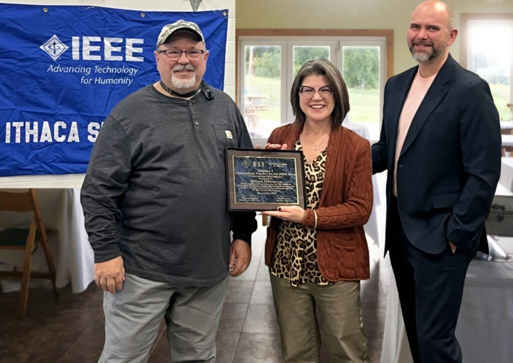 Photo of Dr. Hutchison accepting the 2024 Region 1 Outstanding Teaching In an IEEE Area Award. She is shown with her husband, Steve Hutchison, on the right, and with Mike Joyner, IEEE Ithaca Section Chair. 